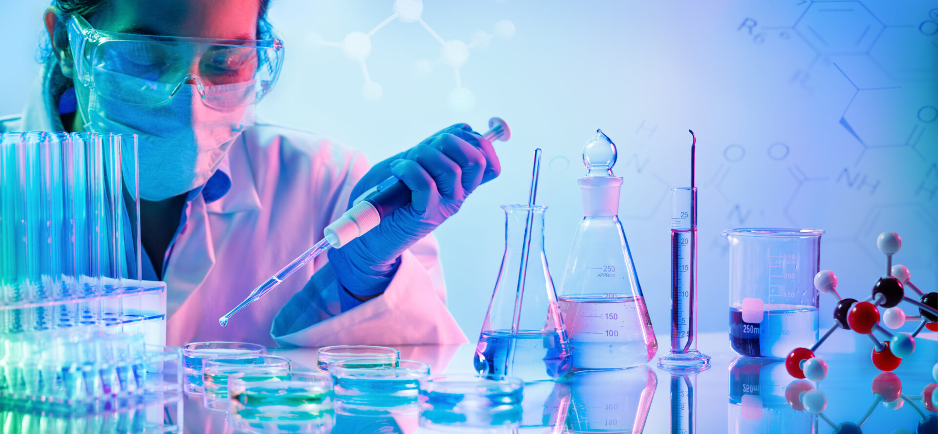 A person in lab coat and gloves holding a pipette.