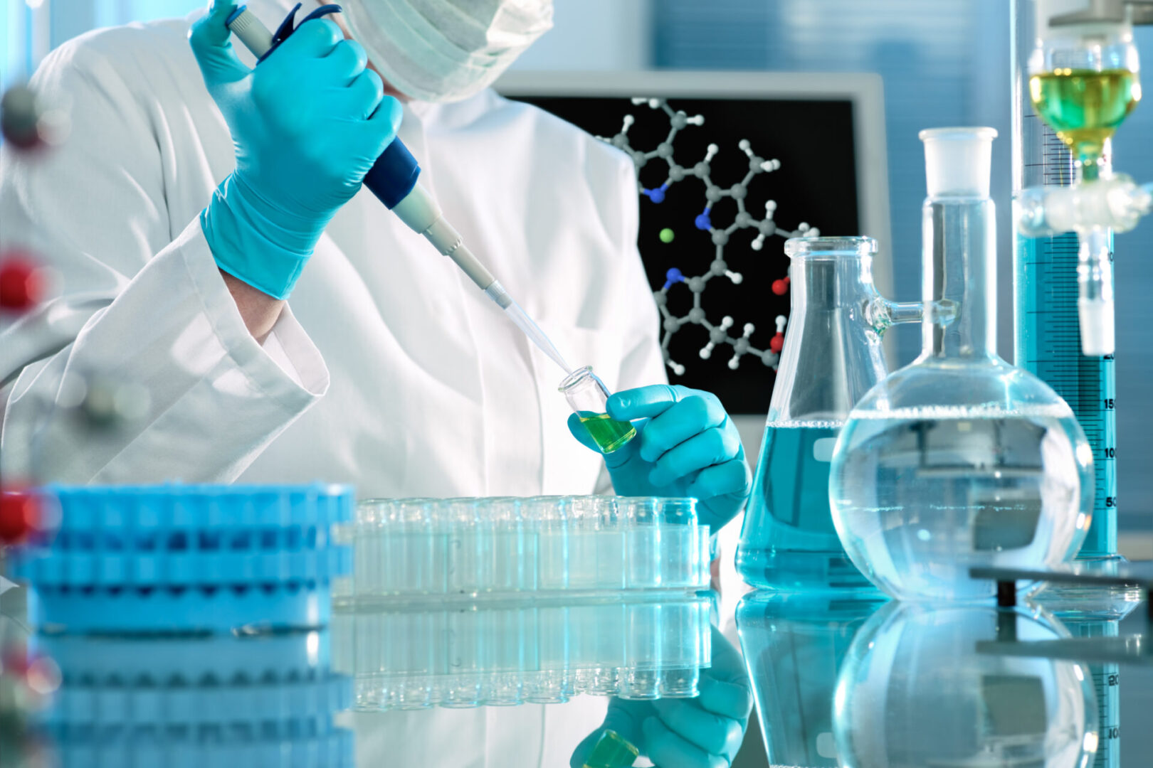 A person in lab coat and gloves working with blue liquid.